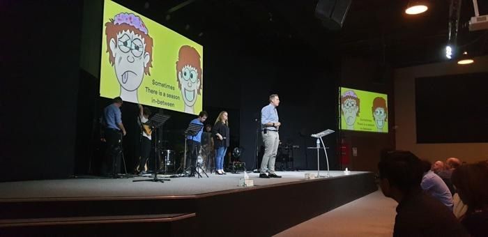 Dave speaking on stage with his cartoons on the big screens